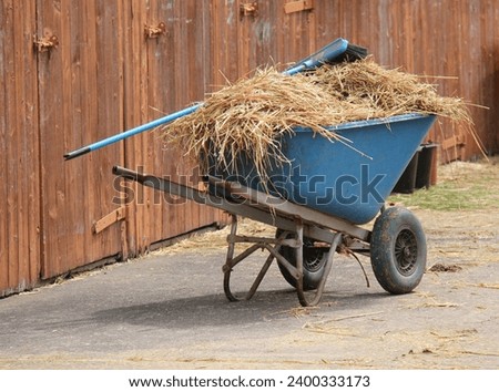 A Wheelbarrow with Straw and a Brush at Horse Stables.