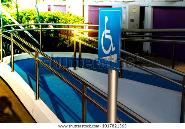 Wheelchair Accessible\
Symbol White on blue Sign /(International) Wheelchair /Blue\
Handicap Symbol/ in front of the  office and   blue footpath  with\
beautufiul color in\
sunset