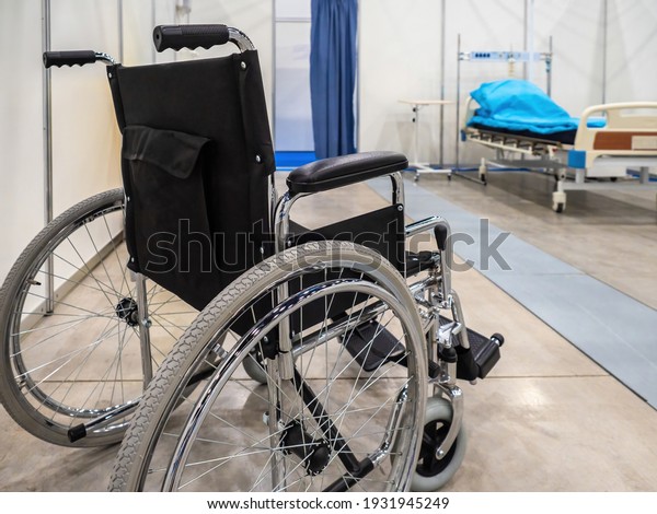 Wheelchair in a hospital ward. Wheelchair on\
wheels. Chair for transporting patients around hospital. Rear view\
of a wheelchair. Concept - sale of hospital equipment. Bed for\
patient in\
background