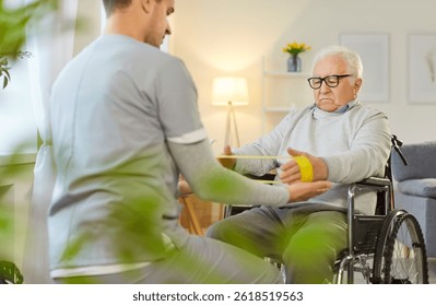 Ejercicios de la banda elástica del hombre sénior de la silla de ruedas para los brazos con el hermano médico, enfermería consultora, atención sanitaria y social de ancianos, médico, enfermera geriátrica masculina que ayuda a la rehabilitación del paciente viejo