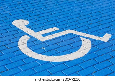 Wheelchair that is a symbolize the parking space for disabled has been painted in blue and white on cobbled road surface.