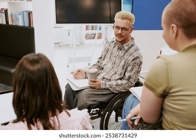 Wheelchair user holding beverage and engaging in group discussion with colleagues in a modern office setting using notebooks and tablets - Powered by Shutterstock