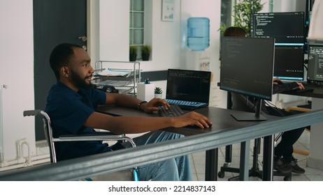 Wheelchair user software engineer working on server program with computer, typing in it coding office. Database programer with chronic disability writing code with system algorithms.