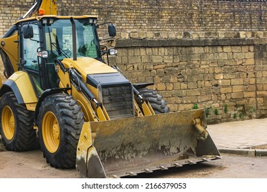 Wheeled Bucket Loader Next To A Brick Wall