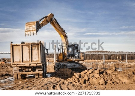 A wheeled excavator loads a dump truck with soil and sand. The excavator digs the ground at the construction site. Removal of soil from a construction site or quarry