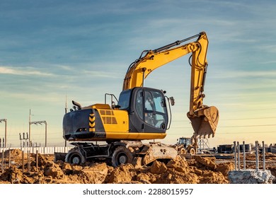 Wheeled works in a pit at a construction site. The excavator carries out excavation work on the background of a cloudy sky. View from the trench. Preparation of a pit for construction