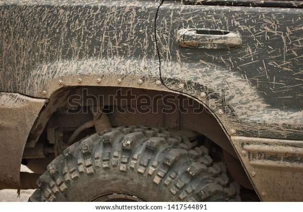 Wheels, lights and bumper are laced in a swamp.\
Dirty parts of a truck close\
up.