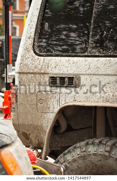 Wheels, lights and bumper are laced in a swamp.\
Dirty parts of a truck close\
up.