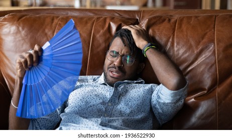 When Ac Is Broken. Overheated Millennial Afro American Man Recline On Couch At Home Get Heat Stroke Use Hand Fan. Sweaty Black Guy Hipster Tired Of Breathing Hot Air Need To Buy Repair Air Conditioner