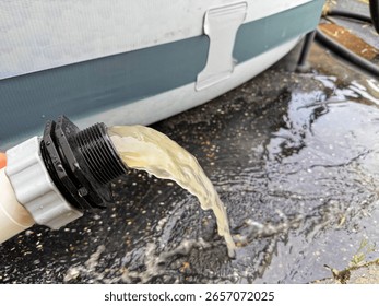 When backwashing the pool water through the sand filter system, dirty, cloudy water comes out of a hose and falls to the ground. During backwashing, the filter sand of the pool filter is cleaned.