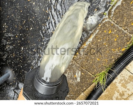 When backwashing the pool water through the sand filter system, dirty, cloudy water comes out of a hose and falls to the ground. During backwashing, the filter sand of the pool filter is cleaned.