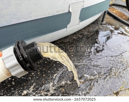When backwashing the pool water through the sand filter system, dirty, cloudy water comes out of a hose and falls to the ground. During backwashing, the filter sand of the pool filter is cleaned.