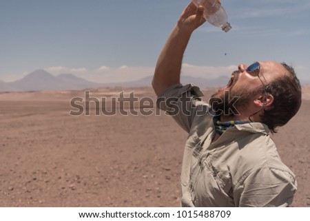 When the desert ties up your throat. The last drop of water in the desert has a bitterweet taste. Male with sunglasses drinking the last waterdrop of the bottle in the driest desert on earth: Atacama