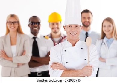 When I grow up I will be a chef. Confident male chef in uniform keeping arms crossed and smiling while group of people in different professions standing in the background
