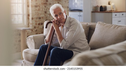 Where Did All The Time Go. Shot Of A Senior Man Sitting Alone On The Sofa At Home And Looking Contemplative While Holding His Walking Stick.