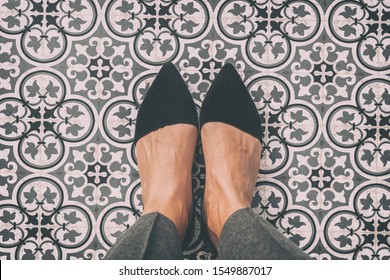 From where I stand first person view perspective of woman standing on tiled floor taking selfie of black suede pointy shoes walking over old fashion ornament pattern tiles in Europe.