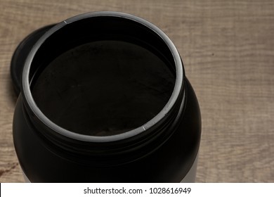 Whey Protein Food Supplement For Training And Exercise. Overhead Of Black Jar And Wooden Table.