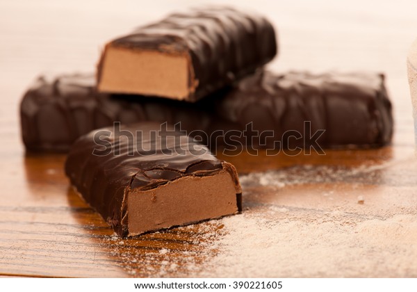 Whey protein powder and chocolate protein bar\
on wooden background.