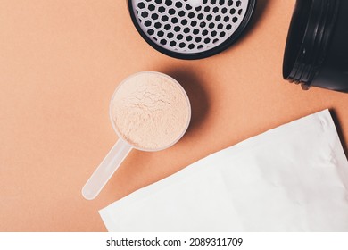 Whey Protein Powder Chocolate Flavor Next To Packaging Paper Bag And Shaker On Brown Background, Top View