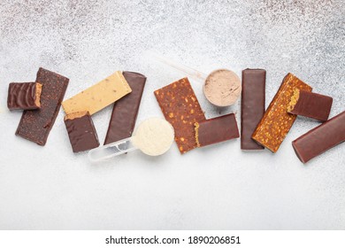 Whey Protein Powder In Measuring Scoop And Different Energy Protein Bar On Grey Background. Top View