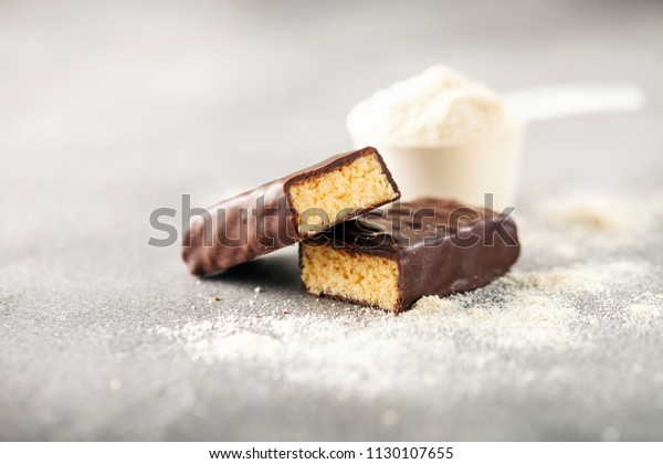 Whey protein powder in measuring scoop and\
energy protein bar on black\
background.