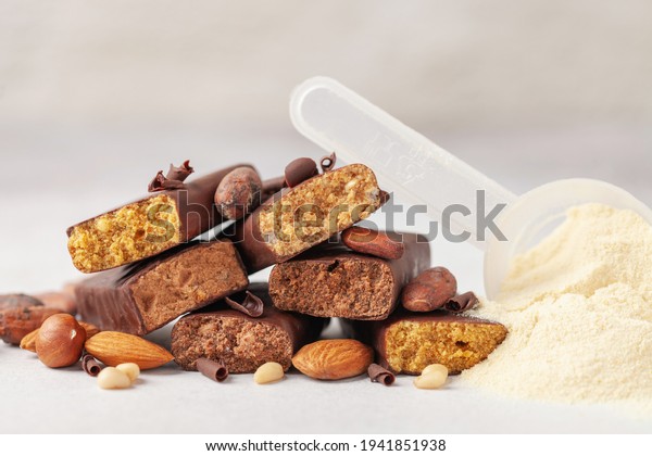 Whey protein powder in
measuring scoop, nuts and different energy protein bar on grey
background.