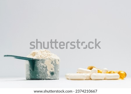 Whey protein powder in measuring spoon, white capsules of amino acids, vitamins and yellow capsules omega 3 on white background, healthy eating and bodybuilding food supplements. 商業照片 © 