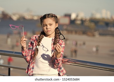 Which Props To Choose. Doubting Small Girl Choosing Glasses Props. Adorable Little Child Holding Photobooth Props On Sticks. Cute Kid With Fancy Party Props On Urban Outdoor.