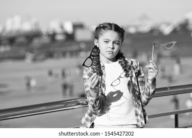 Which Props To Choose. Doubting Small Girl Choosing Glasses Props. Adorable Little Child Holding Photobooth Props On Sticks. Cute Kid With Fancy Party Props On Urban Outdoor.