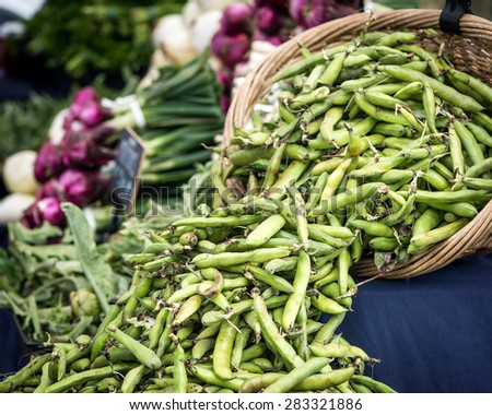 A whicker basket of fava beans at a San Francisco farmer's market.  Onions and other vegetables on a table in the background.