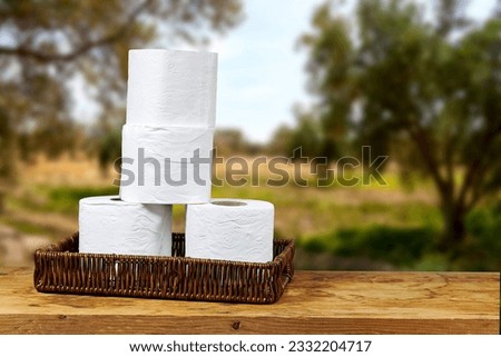 whicker basket with rolls of toilet paper on wooden board table with copy space and near blur olives field background