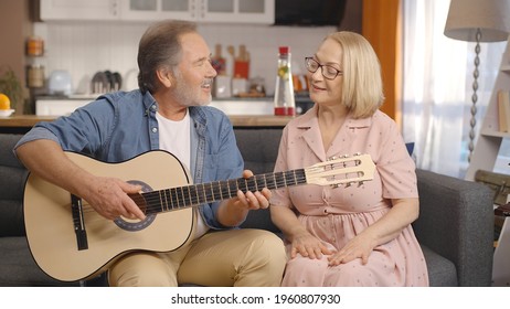 While the bearded old man plays the guitar, his wife gets rhythm with her hands and sings the song.Concept of having fun together, singing with guitar.