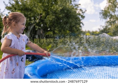 While drawing water into the pool, a happy child closes the hose with his finger and splashes the water. When installing a pool, a lot of splashes fly in all directions. A child plays with water.