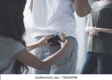 While the parents are standing and talking, the little girl pulls out her father's wallet from his back pocket. From the purse stick money