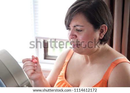 While putting on makeup a beautiful woman looks at her reflection and makes a face. 