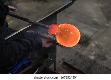 While rolling with a wet newspaper, the shape of a Kosta Boda's drinking glass is applied by hand with liquid glass in a factory in Kosta, Sweden. Red hot orange-red sphere in a glass blowing workshop