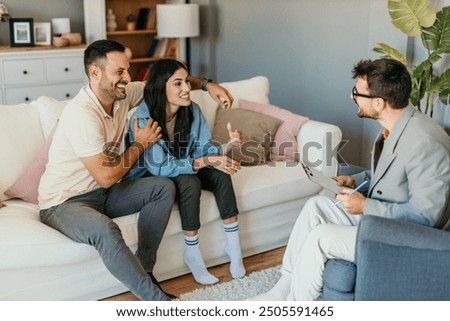 While at their counseling session, the mid adult female smiles and laughs while her husband tells a funny story about how they met.	