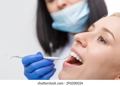 While treating. Close-up of smiling pretty blond-haired woman having her teeth examined by dentist.