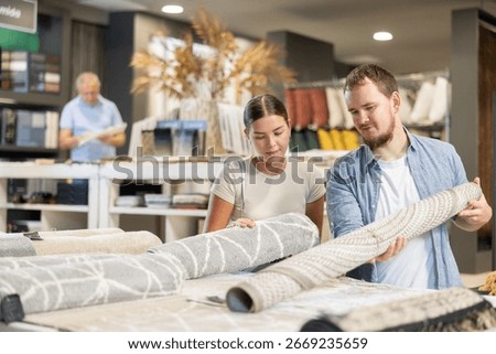 While visiting store of building materials and related household goods, guy with wife choose carpet. They examines and touches product options, thinks about buying