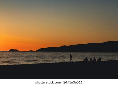 While watching the evening sunset on the shores of Agawa Bay campground a silhouetted young woman takes a photograph of her family while they all relax along the beach - Powered by Shutterstock