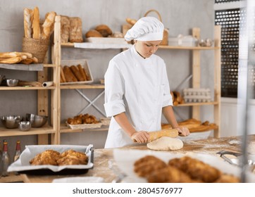 While working in bakery using rolling pin, girl cook makes thin flat cakes from dough with rolling pin, prepares dough for baking croissants.