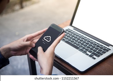 While working on laptop man doing cloud uploading on his smartphone at outdoor cafe - Powered by Shutterstock