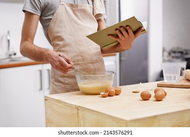 Whipping up a quick meal. Cropped shot of a young man cooking in the kitchen with the help of a cookbook. - Powered by Shutterstock