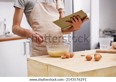 Whipping up a quick meal. Cropped shot of a young man cooking in the kitchen with the help of a cookbook.