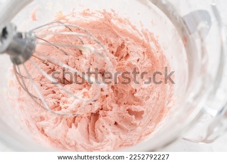 Whipping strawberry buttercream frosting in a stand-alone electric mixer with a whisk attachment.