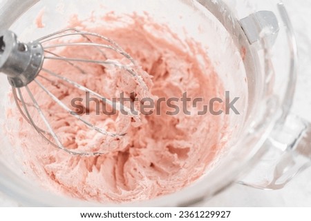 Whipping strawberry buttercream frosting in a stand-alone electric mixer with a whisk attachment.