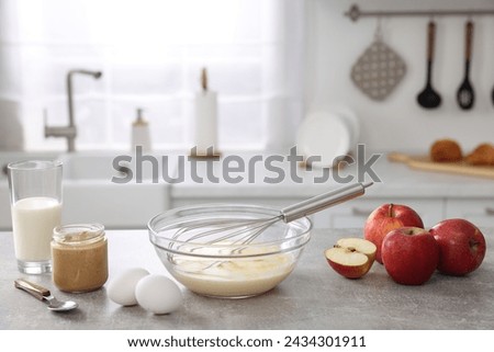 Whisk, bowl, beaten eggs and other ingredients on grey table indoors, space for text
