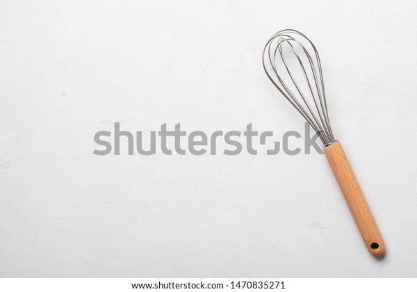 Whisk cooking egg beater mixer\
whisker new clean with wooden handle on stucco table top\
view