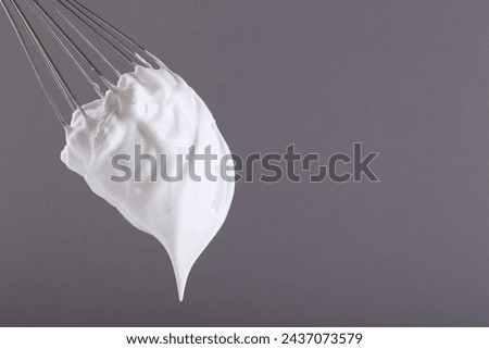 Whisk with whipped cream on grey background. Space for text