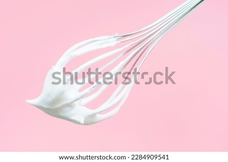 Whisk with whipped cream on pink background close-up.